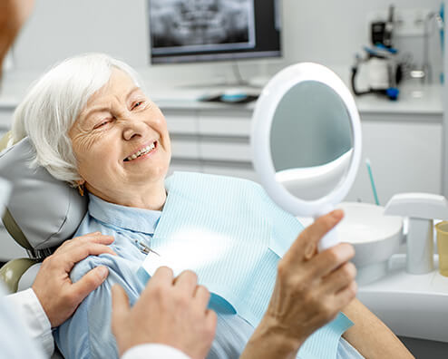 senior woman sitting in a dental chair, looking at her smile in a mirror