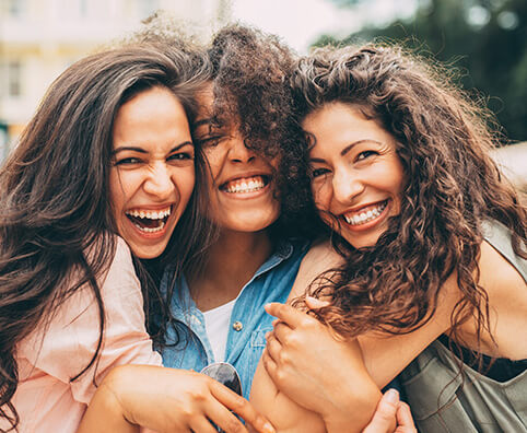 group of three female friends smiling and hugging