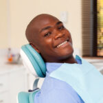 Black bald man smiles while sitting in a dental chair before his dental checkup