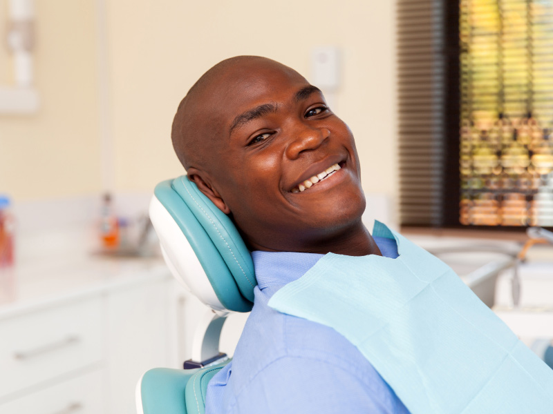 Black bald man smiles while sitting in a dental chair before his dental checkup